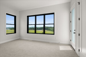 empty bedroom with black frame windows and green meadow mountain view
