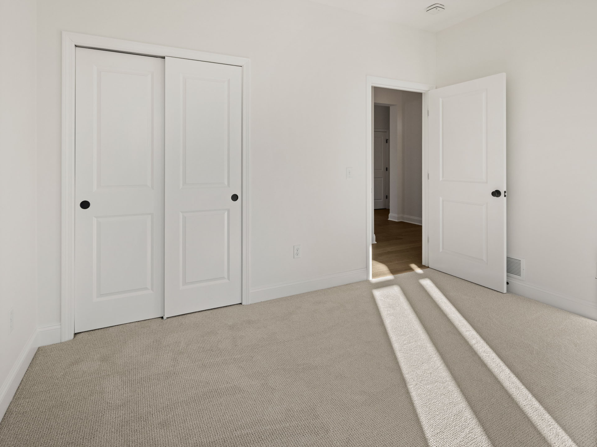 empty bedroom with sliding closet doors and hallway view
