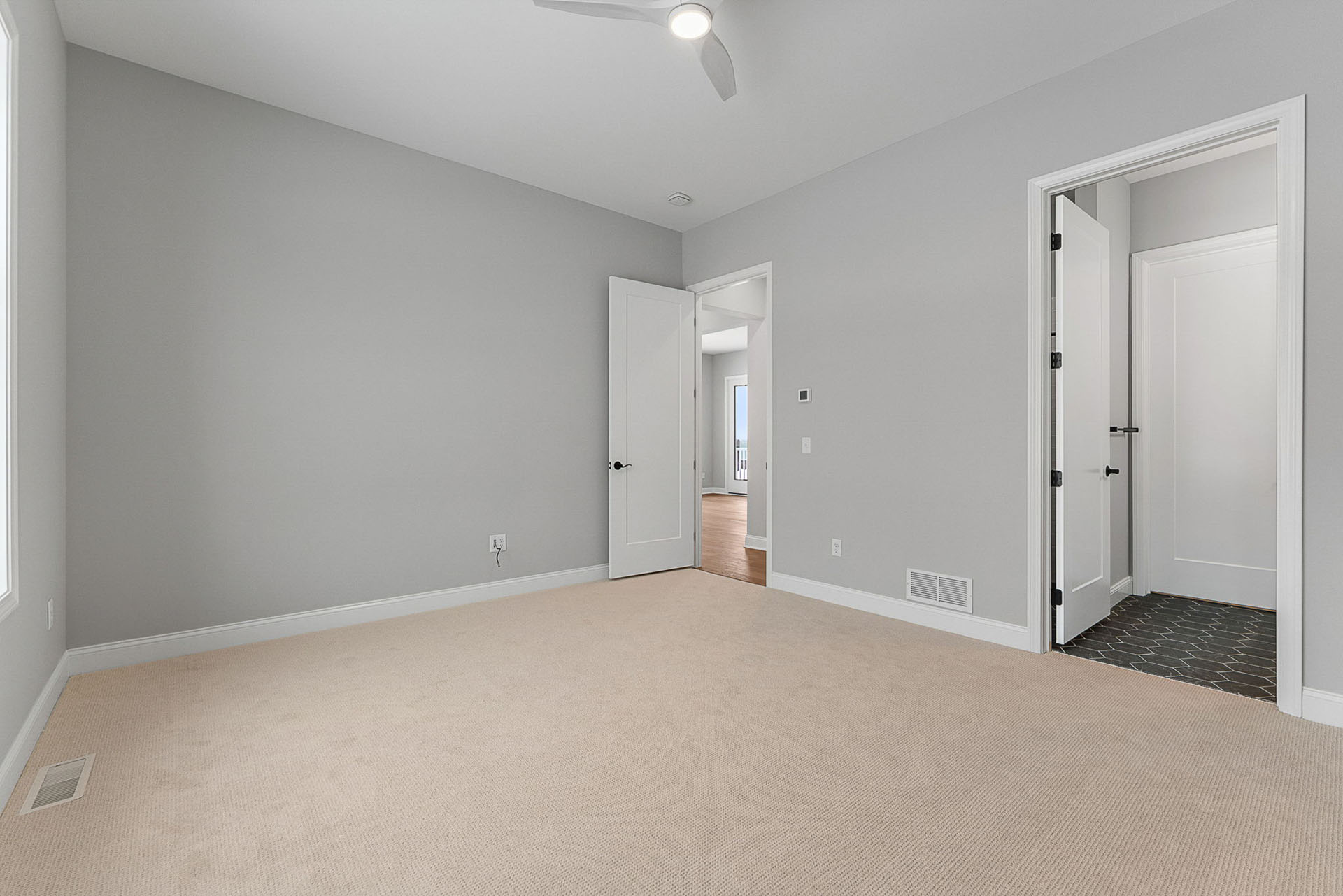 empty gray bedroom with ceiling fan and en suite bath door