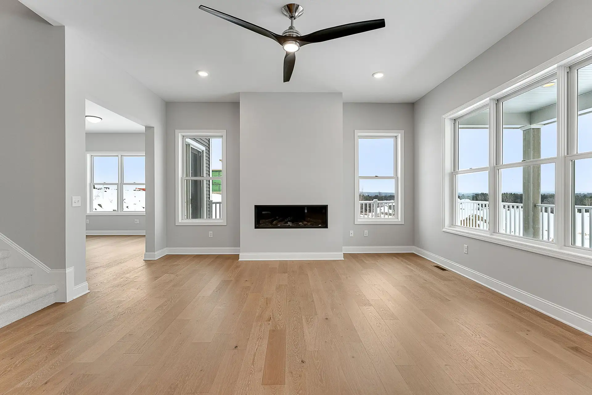 empty living room with linear fireplace ceiling fan and staircase
