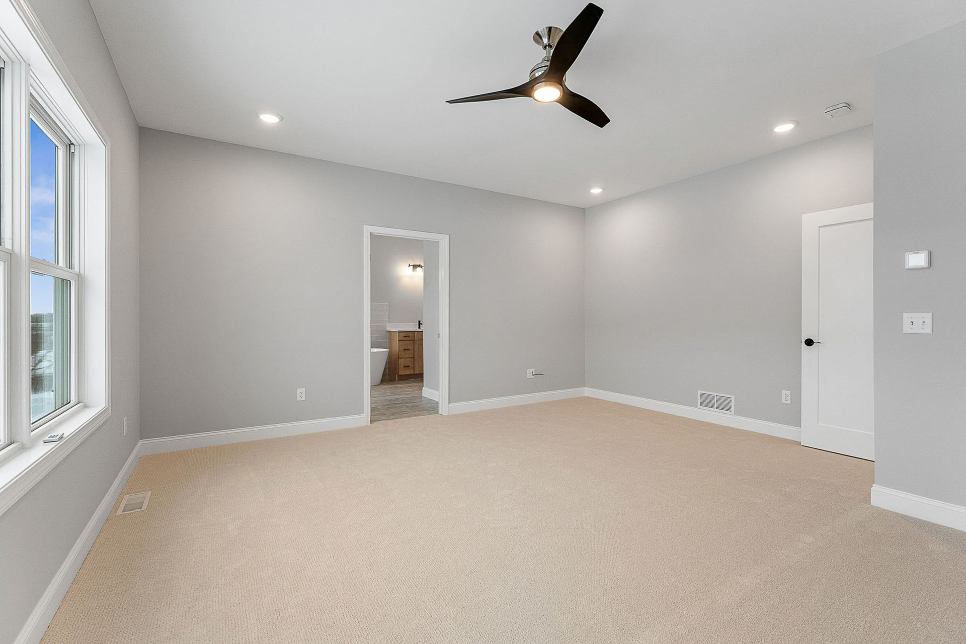 empty primary bedroom with black ceiling fan and en suite doorway