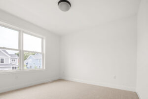empty white bedroom with corner window and blue house street view