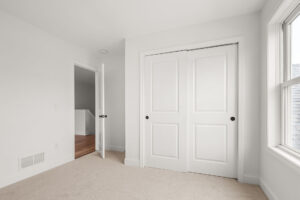 empty white bedroom with sliding closet and hallway staircase view