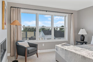 gray bedroom with triple window sky view and lounge chair.