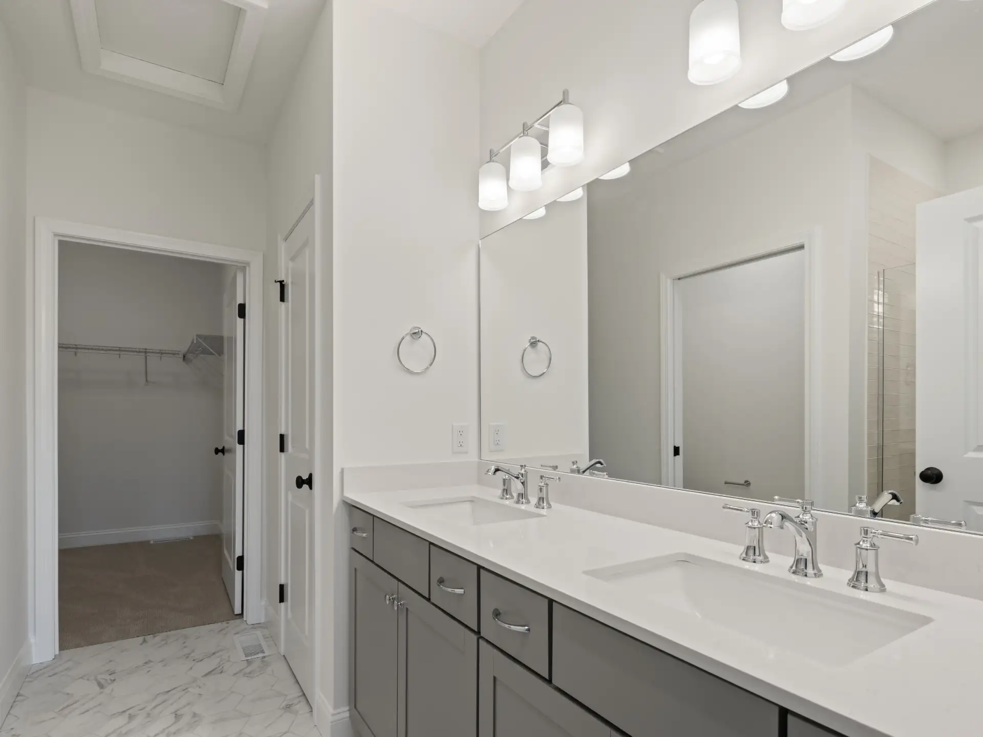 gray double vanity with marble floor and walk in closet door