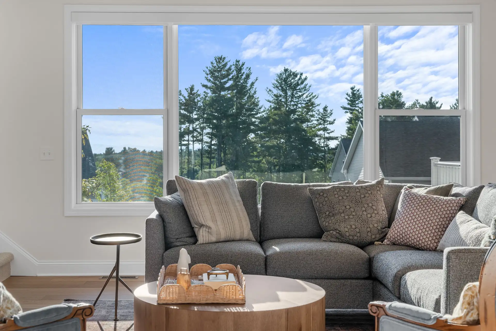 living room gray sectional with triple window and pine tree view