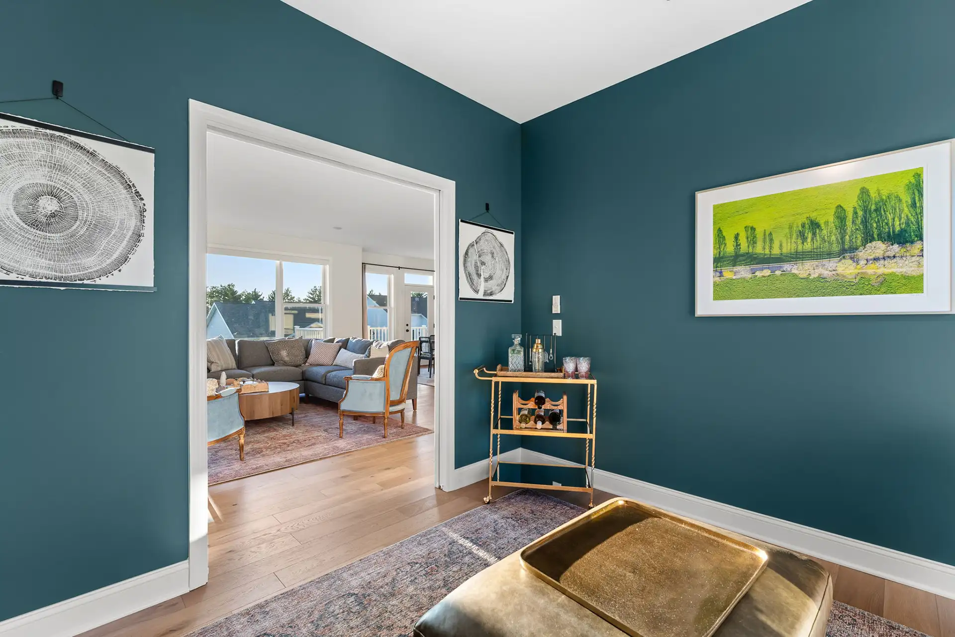 teal room with gold bar cart and open doorway to bright living room