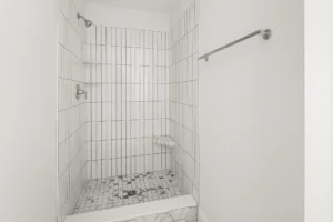 vertical white tile shower stall with mosaic floor and corner shelf