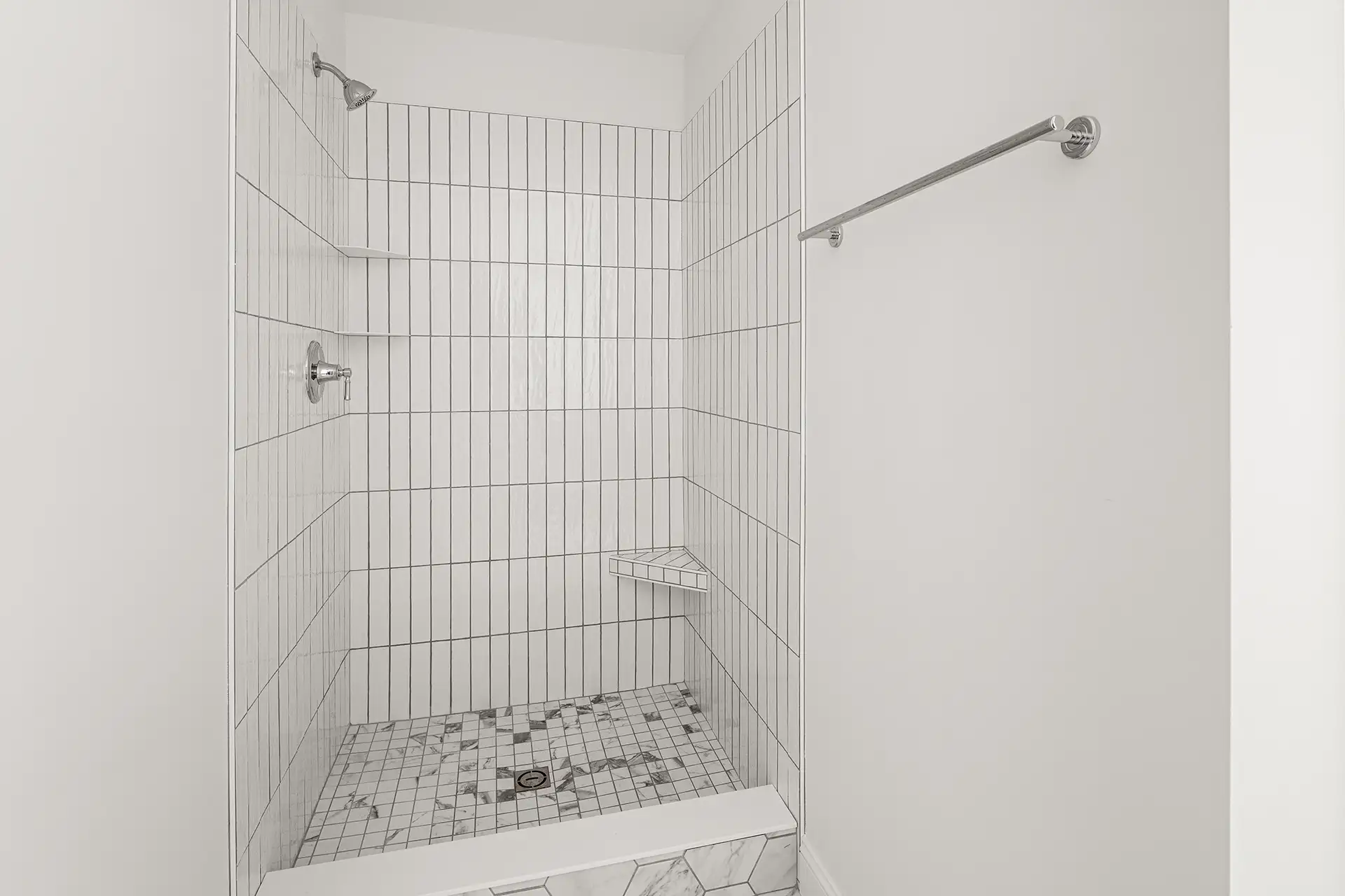 vertical white tile shower stall with mosaic floor and corner shelf