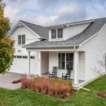 white farmhouse side angle with black rockers and autumn tree