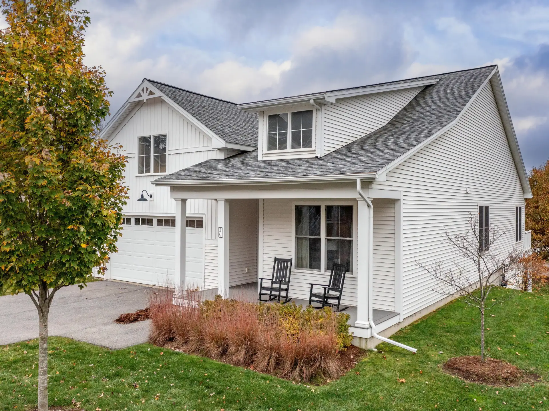 white farmhouse side angle with black rockers and autumn tree