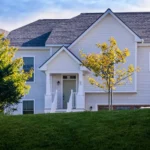 white shingle home facade with gabled entry and young trees