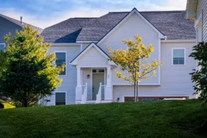 white shingle home facade with gabled entry and young trees