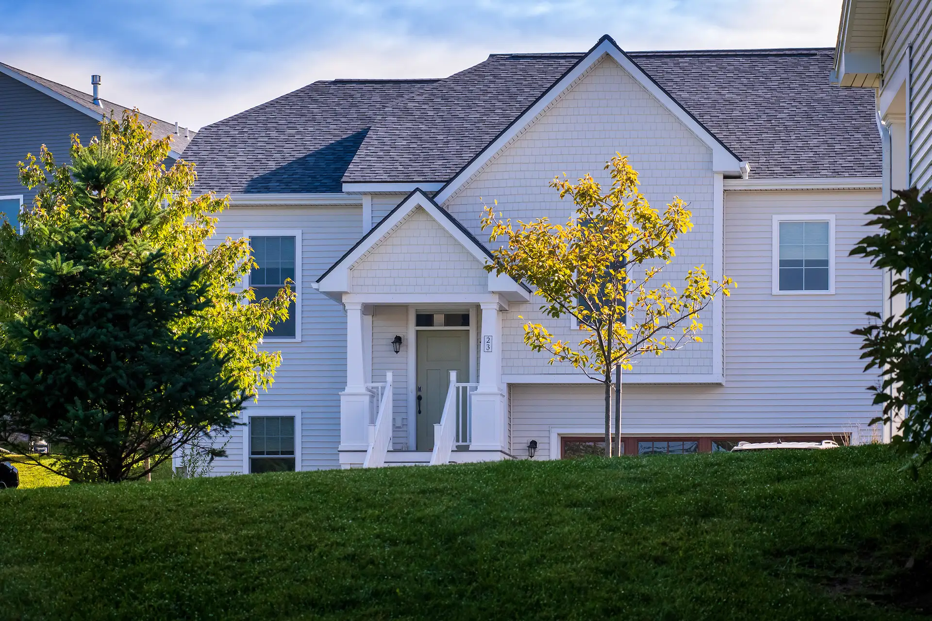 white shingle home facade with gabled entry and young trees